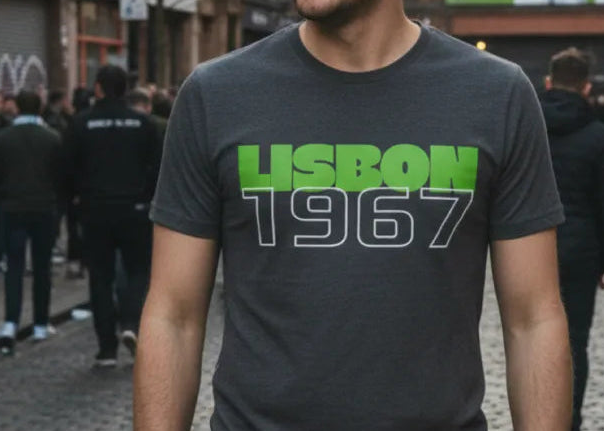 Man wearing a 'Lisbon 1967' t-shirt standing on a street with a large screen in the background showing sports event.