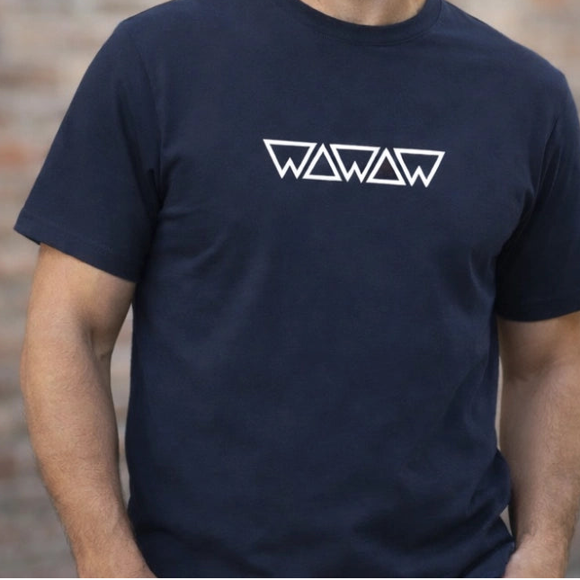 Man wearing a navy blue t-shirt with a logo against a brick wall.